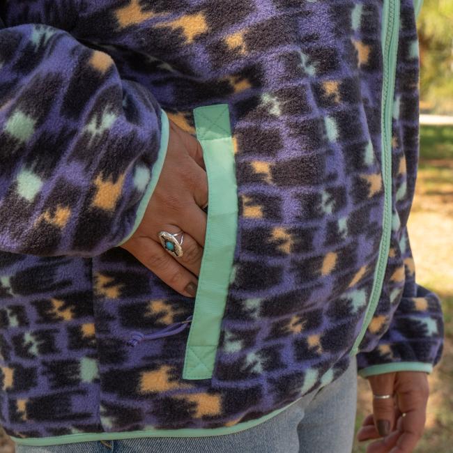 A person in a Patagonia W Purple Pattern Zip Jacket rests their hand by the pocket, also wearing a silver ring with a blue stone.