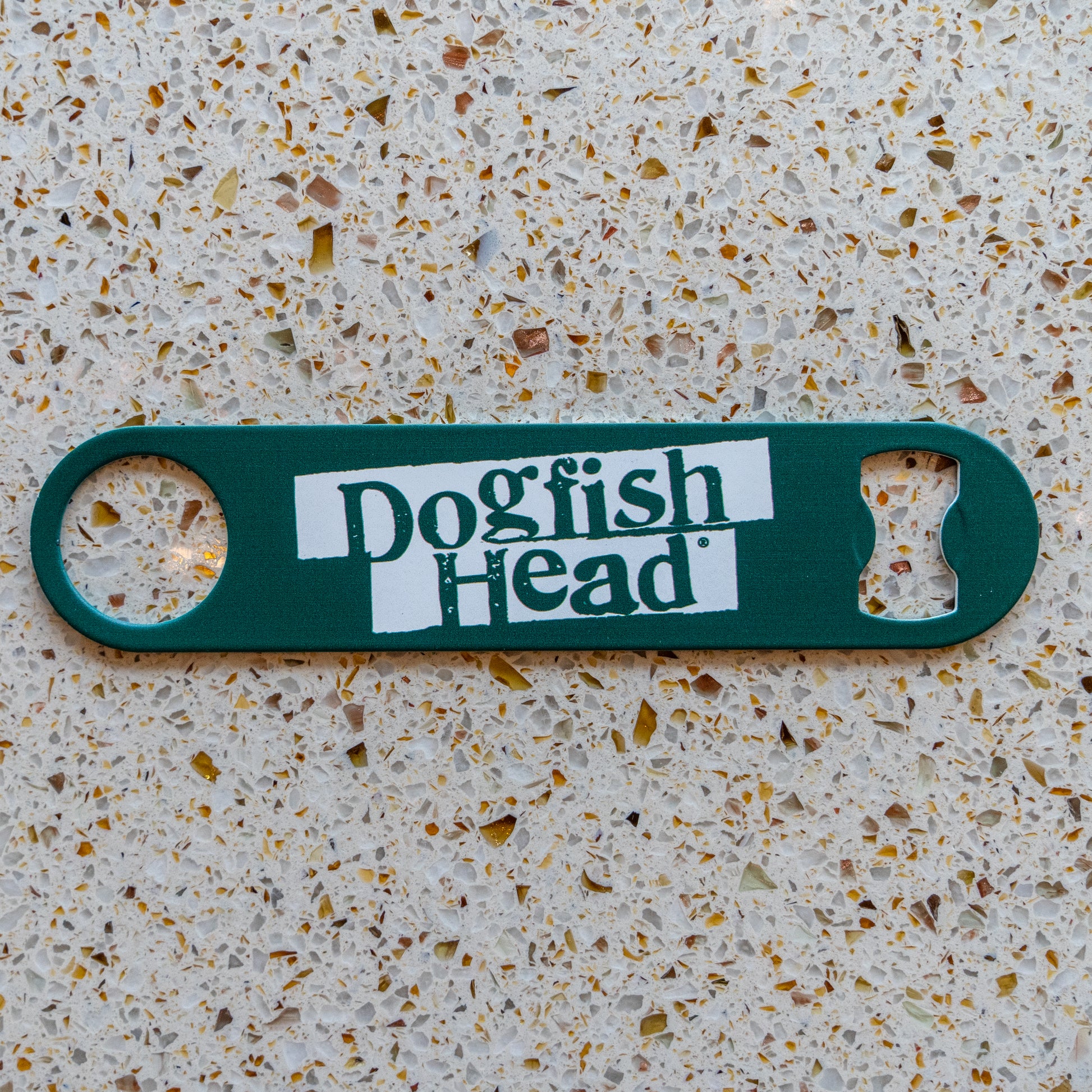 A green Merchtank Bartender Opener with white branding rests on a speckled beige countertop.