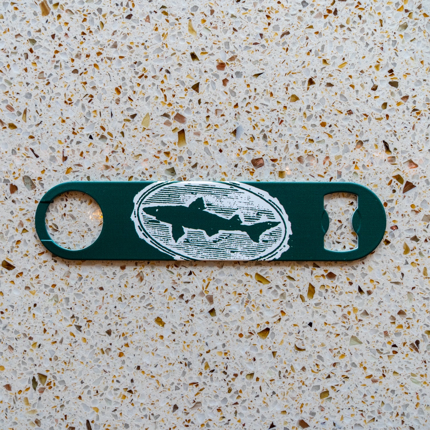 The Merchtank Bartender Opener features a green body with a white fish and oval logo, displayed on a speckled, light-colored countertop.