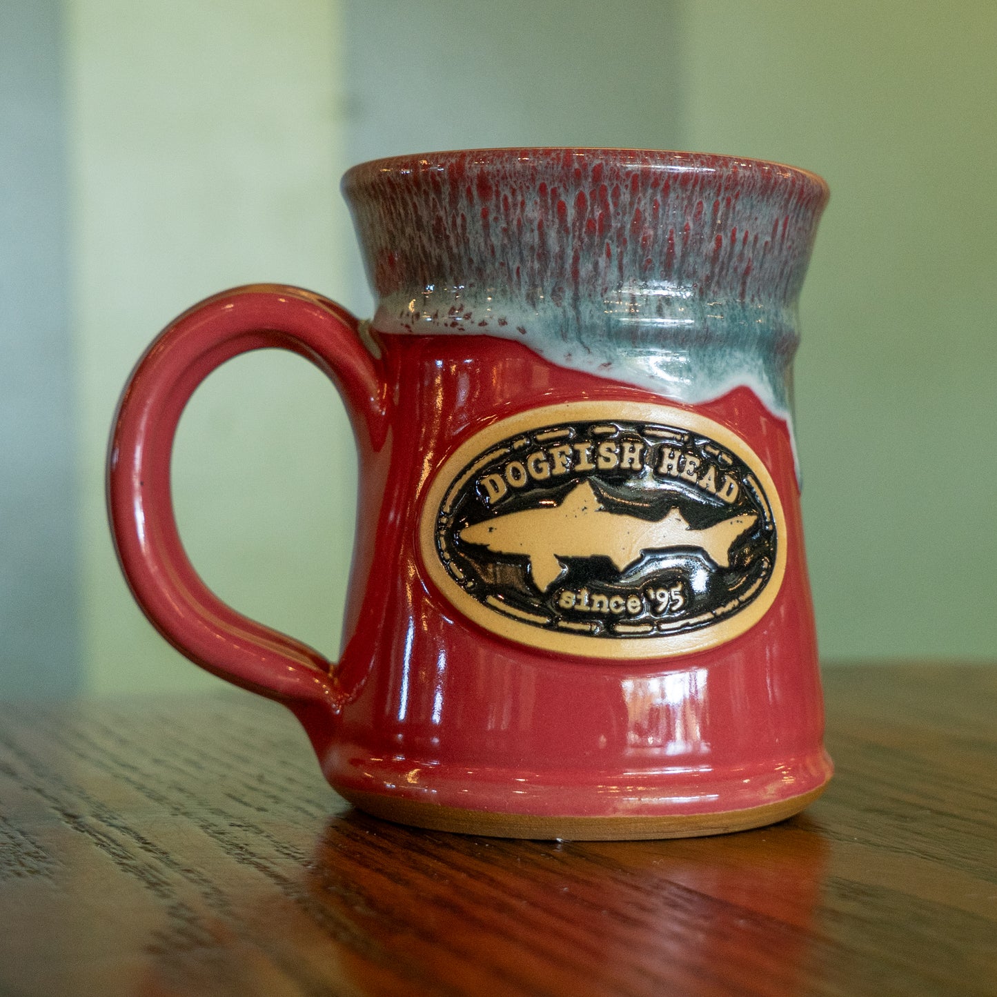 A pink Analog Splitrock ceramic mug by Deneen Pottery, with a sturdy handle, blue-gray rim, and "Analog Splitrock" logo sits on a wooden surface—an ideal way to show your style.