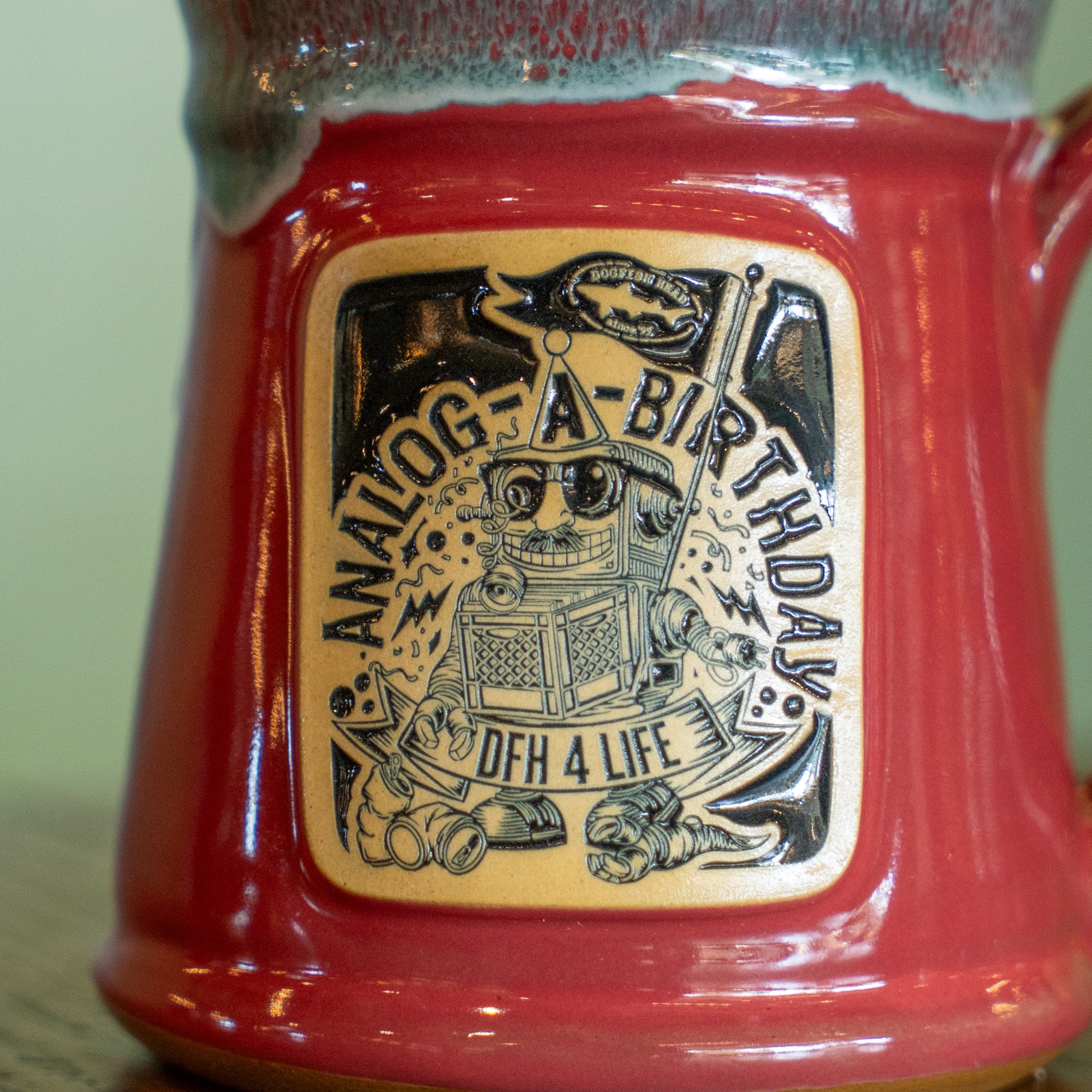 The Pink Analog Splitrock Ceramic Mug by Deneen Pottery features a playful label with a cartoon robot holding a flag, “ANALOG-A-BIRTHDAY,” “DFH 4 LIFE,” lightning bolts, and a horn—a fun celebration of brewery pride.