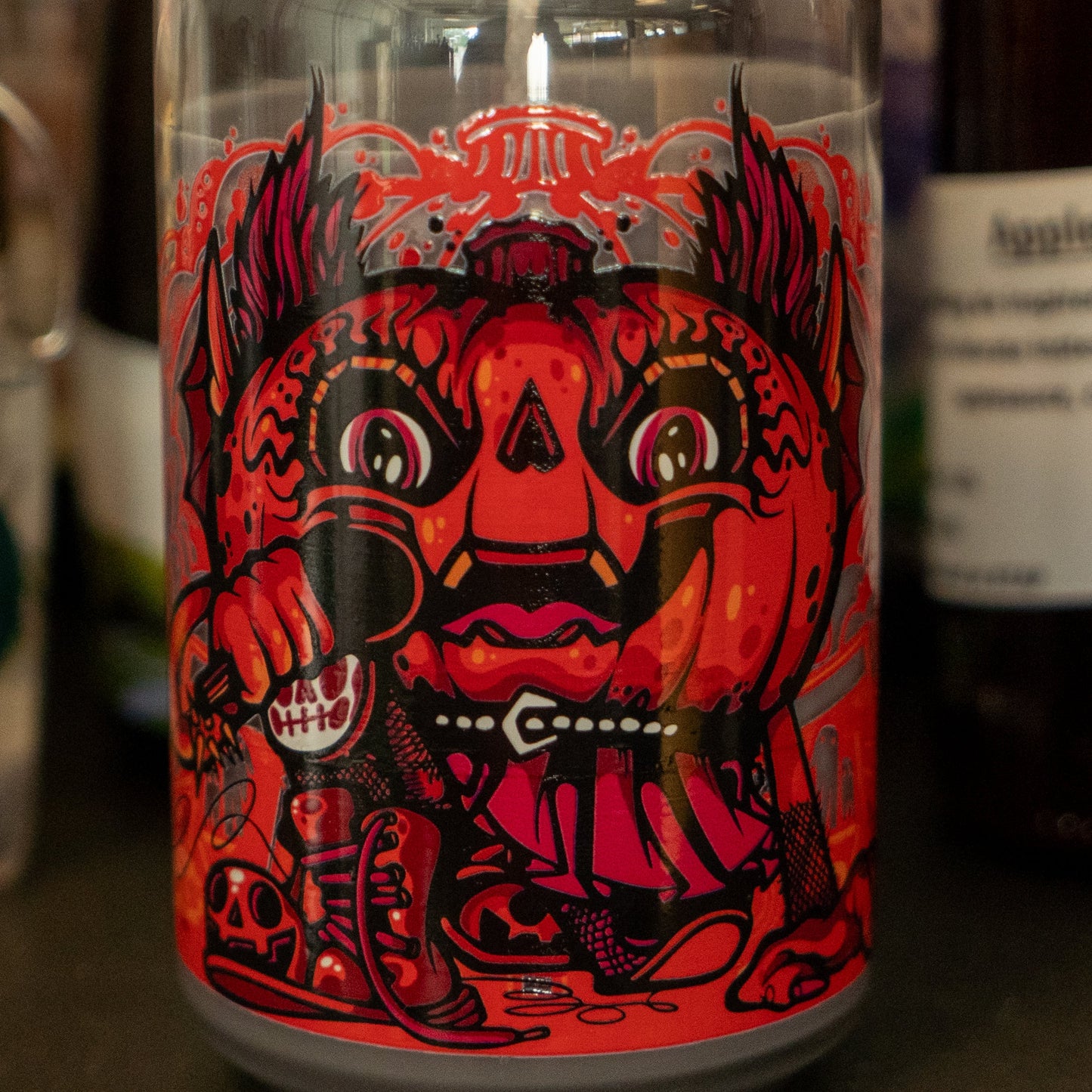 The Punkin Can Glass Candle by Unwined Candles, LLC features bold artwork of a fierce, fanged pumpkin with red eyes and claws in red, black, and orange—perfect for fall with its warm pumpkin spice scent.
