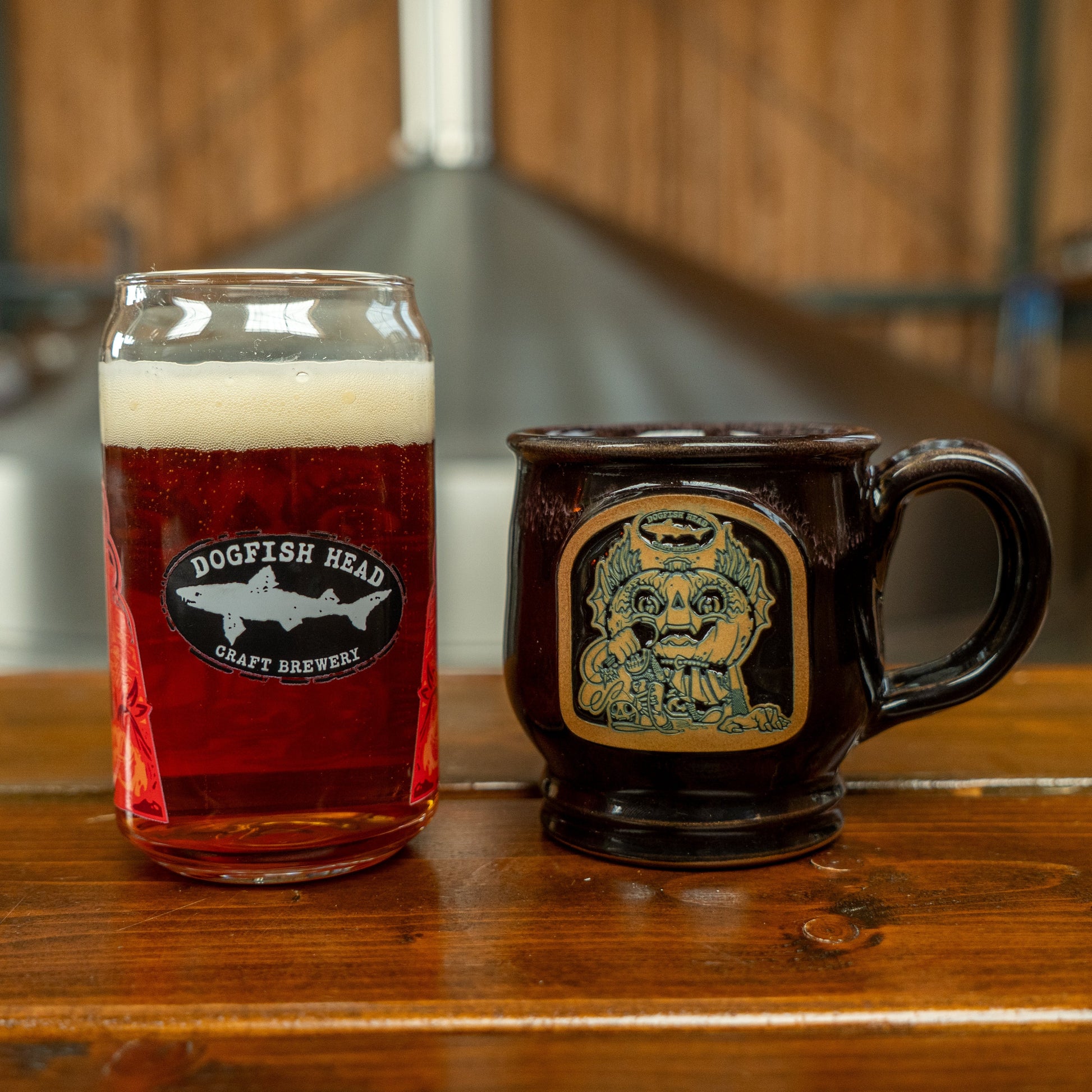 Image of Punkin can glass and mug next to each other. This side of the can glass features the black and white Dogfish Head shark and shield logo. The mug features punkin artwork in brown and black.