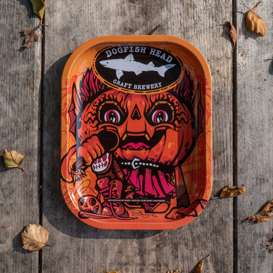 The Punkin Metal Trinket Tray from Rollyourownpapers.com features a vibrant, cartoon pumpkin-head character holding utensils on a rustic autumn background—perfect for seasonal decor.