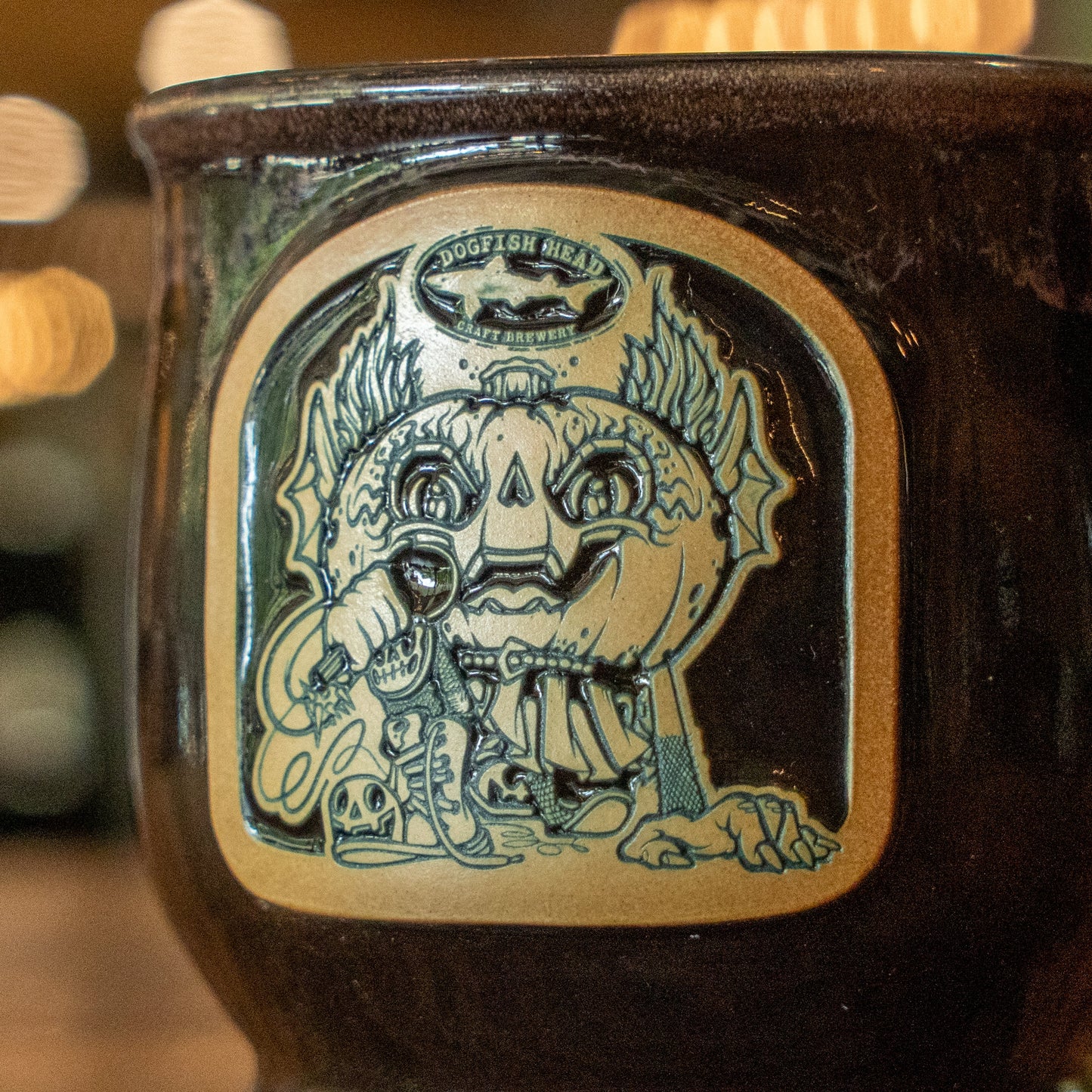 The Punkin Mug Candle by Unwined Candles, LLC is a ceramic autumn mug engraved with a whimsical pumpkin-headed creature and Dogfish Head above—perfect for cozy seasonal sips.