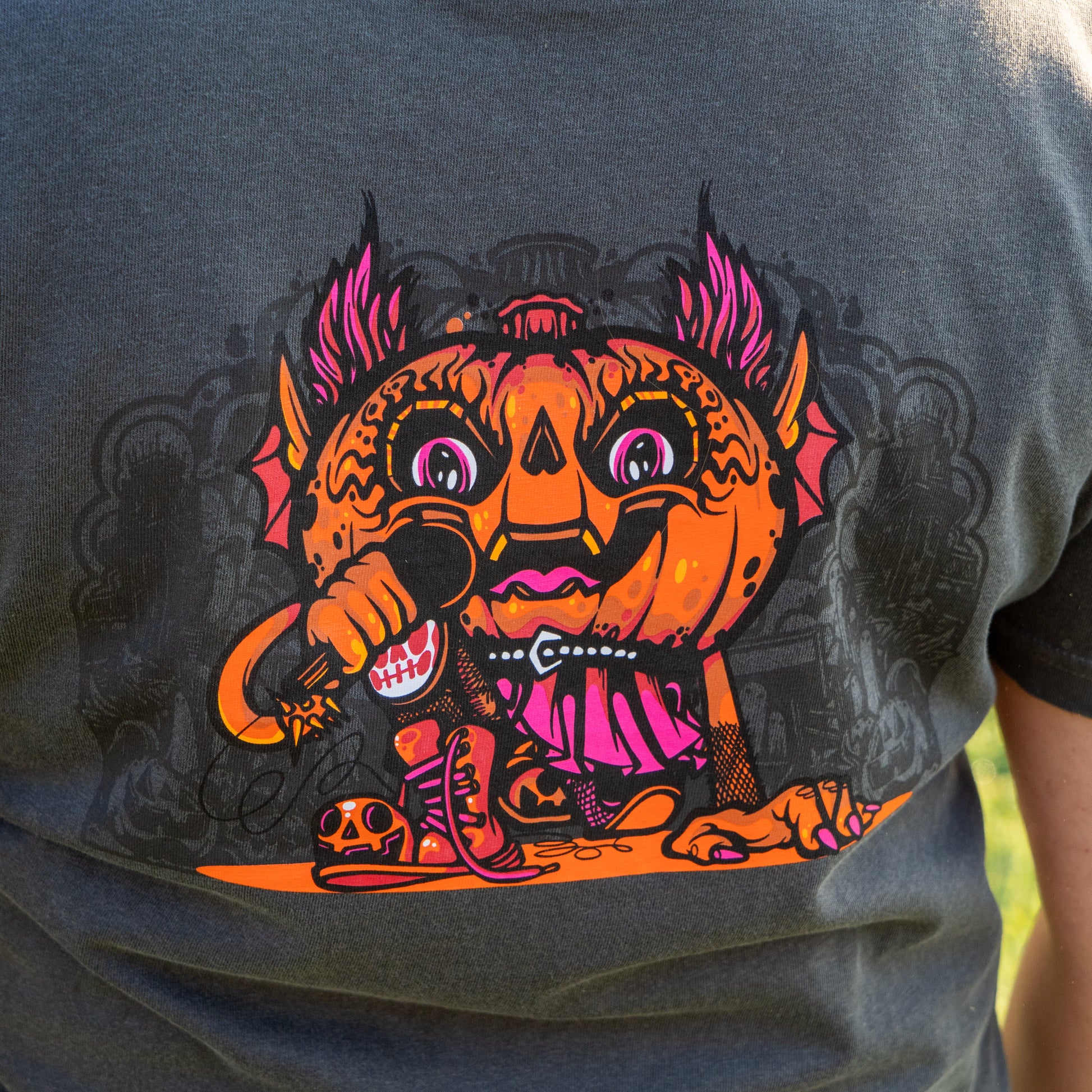 A close-up of the GO WEST T-SHIRT COMPANY's Punkin Short Sleeve Tee, featuring a vibrant cartoon pumpkin with bat wings and a mic, set against bold designs on a dark backdrop—your must-have seasonal shirt!.