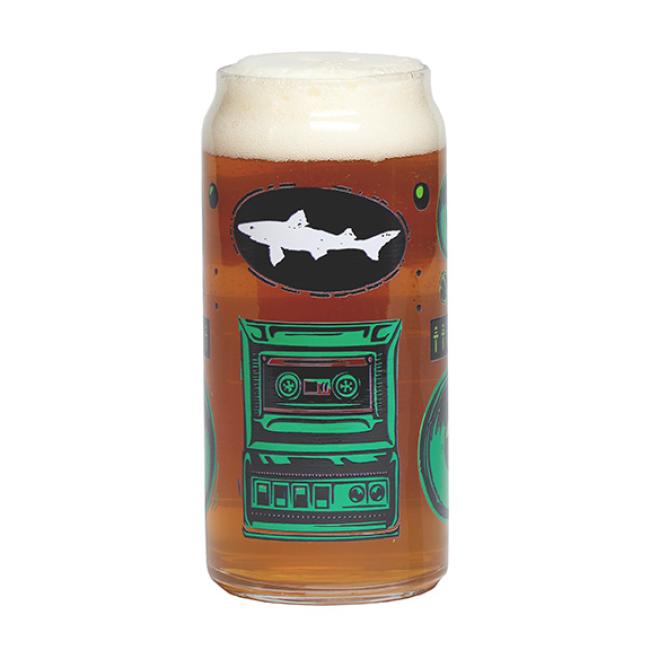 Enjoy your amber beer in the Retro Stereo Tall Boy Can Glass by Grandstand Glassware & Apparel, featuring colorful graphics like a white shark and green cassette tape with a foamy head for added style.