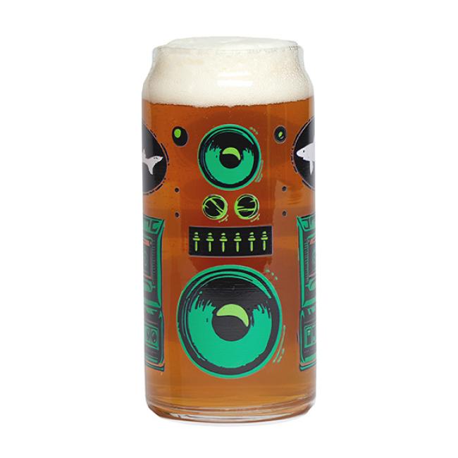 A glass of beer with a thick foamy head and illustrations of green and black speakers captures the vibe of the Retro Stereo Tall Boy Can Glass by Grandstand Glassware & Apparel—perfect for music and beer lovers.