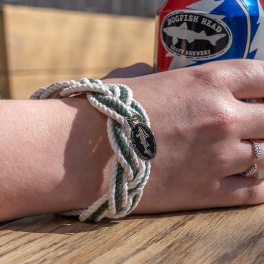 White and green intertwined rope bracelet with a charm attached. Charm is an oval Dogfish Head shark and shield logo.
