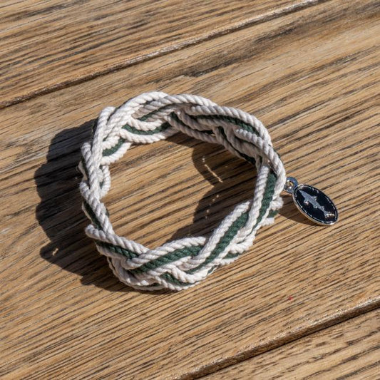 White and green intertwined rope bracelet with a charm attached. Charm is an oval Dogfish Head shark and shield logo.