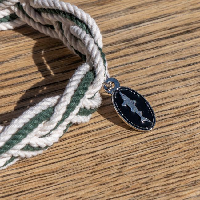 White and green intertwined rope bracelet with a charm attached. Charm is an oval Dogfish Head shark and shield logo.