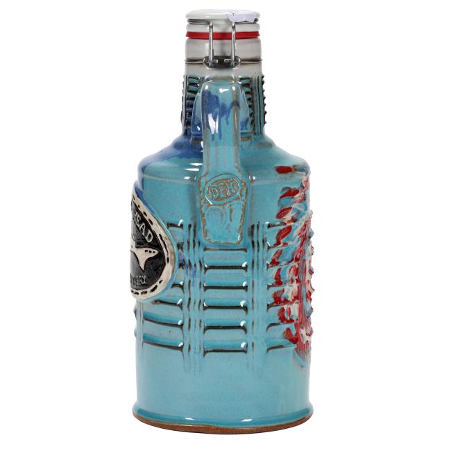 The Tie Dye Ceramic Growler by Romanick Pottery is a blue handcrafted beer growler featuring a handle, metal clasp lid, and intricate molded designs, including a badge-like emblem and a raised decorative side pattern.