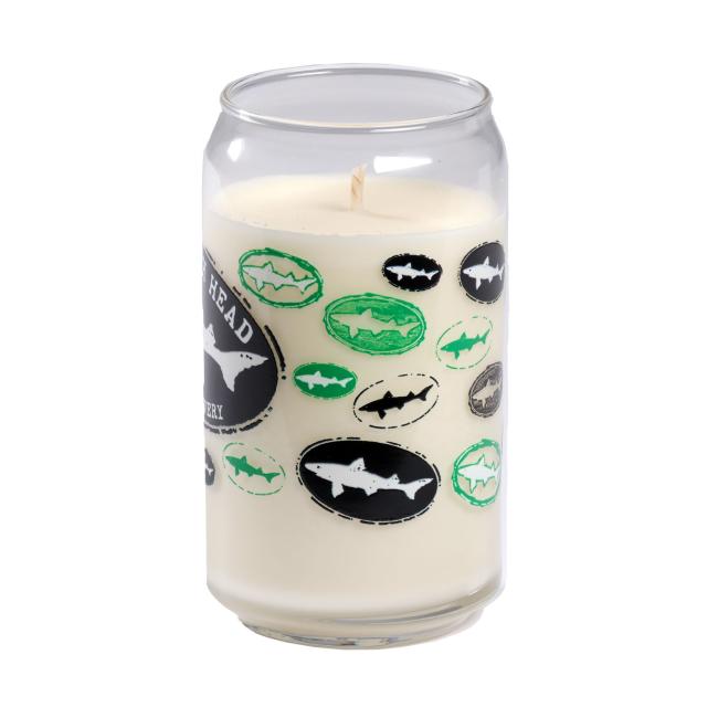 The Vanilla Core Logo Candle by Unwined Candles, LLC is a vanilla-scented candle in a reusable soda can-shaped glass holder, decorated with green, black, and white ovals featuring shark silhouettes.