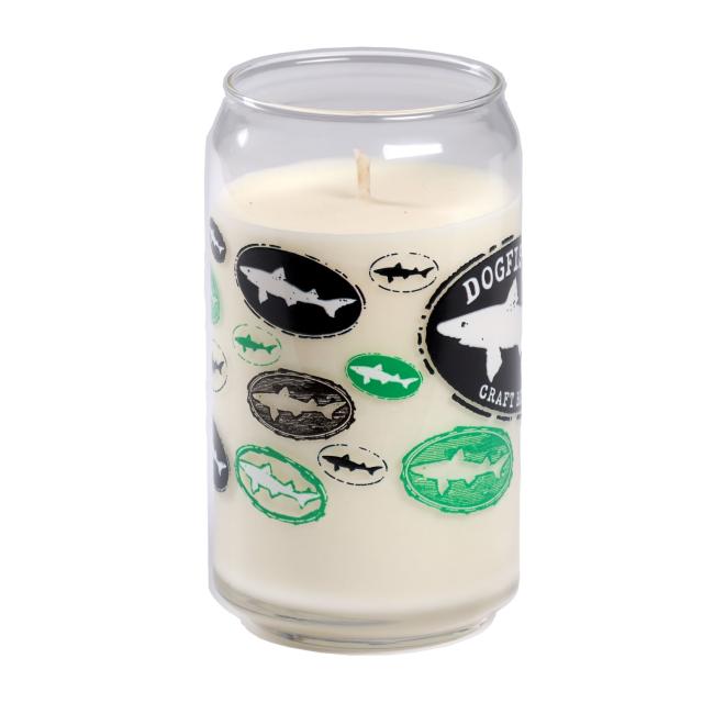 The Vanilla Core Logo Candle by Unwined Candles, LLC is a vanilla-scented candle in a reusable, soda can-shaped clear glass with green, black, and gray shark-logo ovals and "Dogfish Head Craft Brewed" text.