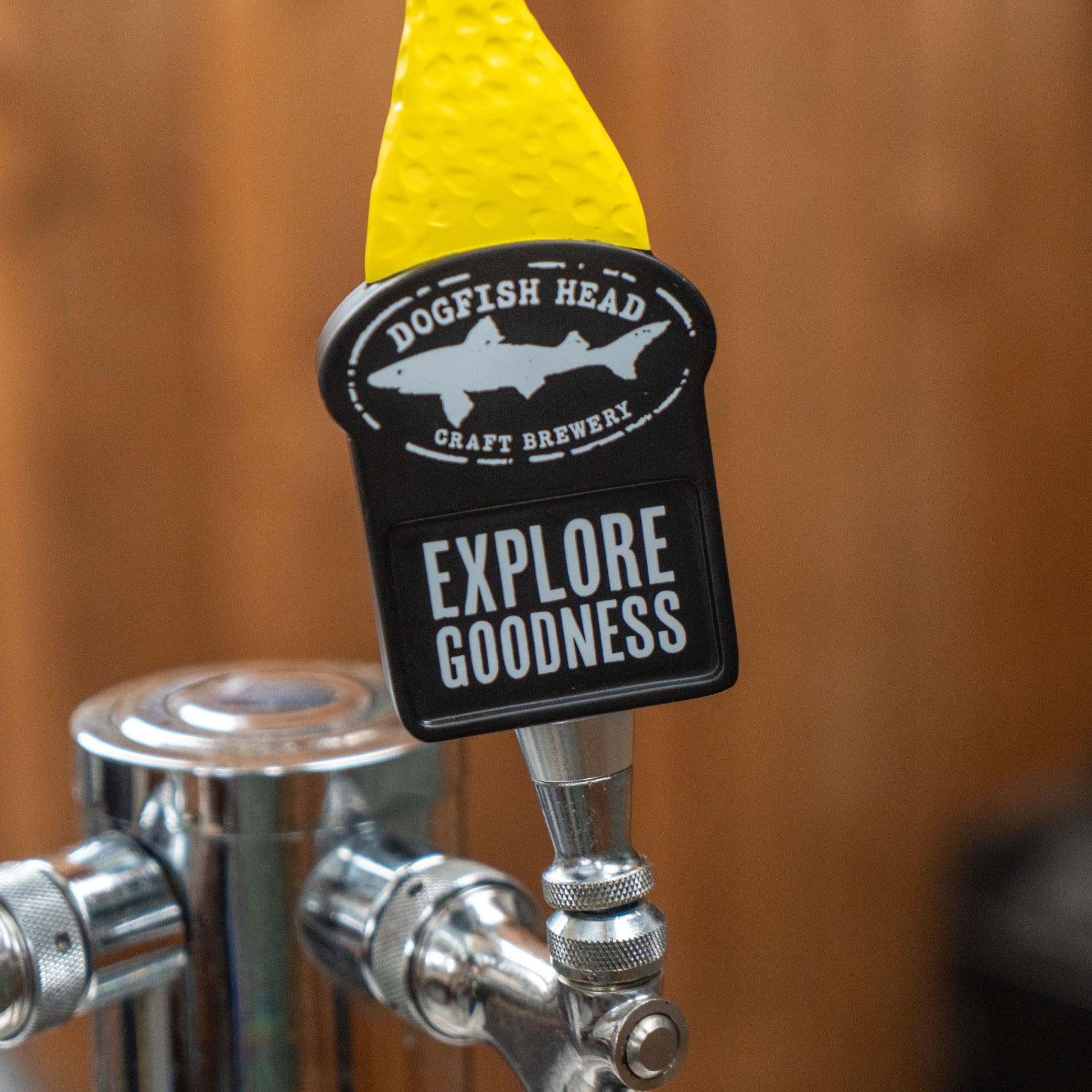 Close-up of a neon yellow Yellow Shark Tap Handle by Merchtank, set against a blurred wooden background.