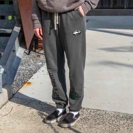 Front view of sweatpants being modeled. Top left of pant features the Dogfish Head shark and shield logo. Bottom left of pant features a green hop cone graphic. Right side of pant features writing "GOT A MINUTE?" going upward from the ankle.