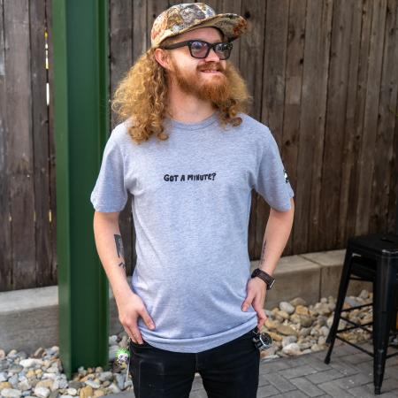 Tee being modeled, the front features writing "Got A Minute?" in black.