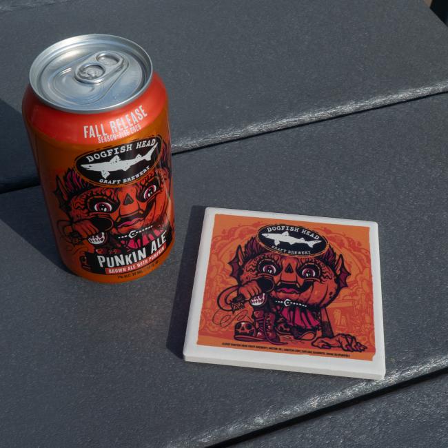 Image of the Dogfish Head Punkin Ale with the coaster. Orange coaster with white border. Coaster has Punkin artwork on it with the Dogfish Head shark and shield logo up top.