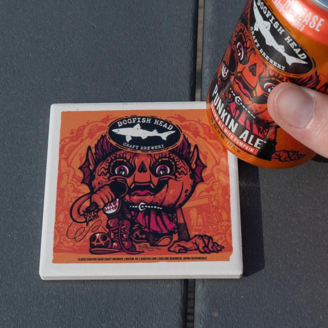 Image of the Dogfish Head Punkin Ale with the coaster. Orange coaster with white border. Coaster has Punkin artwork on it with the Dogfish Head shark and shield logo up top.