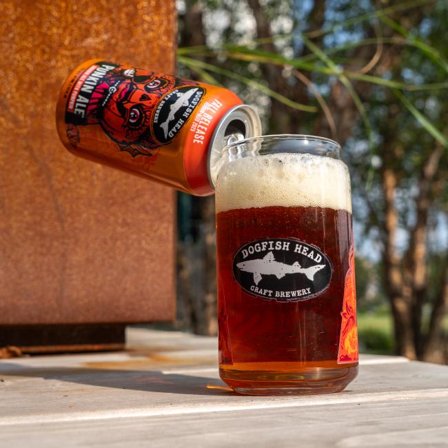 Back view of the can glass which features the Dogfish Head shark and shield logo with a Punkin Ale can being poured into the glass.