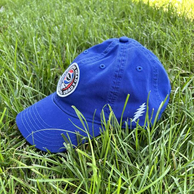 Front view of royal blue hat shown laid on grass. Hat features Dogfish Head x Grateful Dead collaboration logo emblem centered to front of the hat.