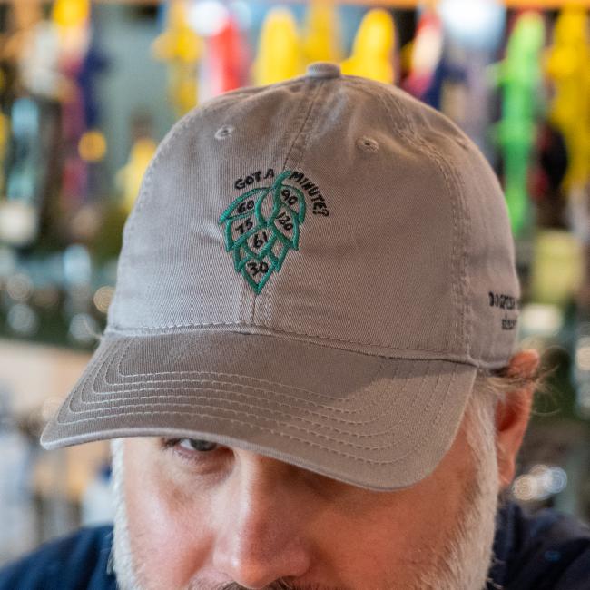 Close-up of front of grey hat features a green hop cone graphic with numbers '60', '90', '75', '120', '61' and '30' inside it, and the text 'GOT A MINUTE?' above it.