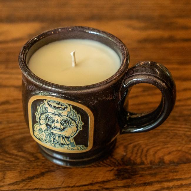 Image of black mug filled with candle. Mug has brown and black Punkin artwork on the front of it.