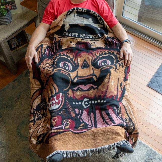 Blanket shown on wearing, features pumpkin artwork and Dogfish Head shark and shield logo.