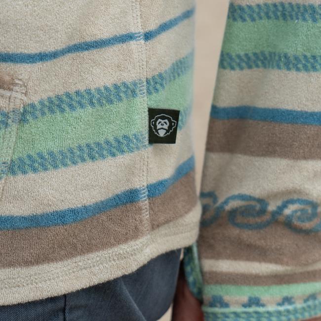 Male model wearing Howler collaboration multi stripe terry cloth stripe hoodie. Close up of small black Howler tag on side seam. 