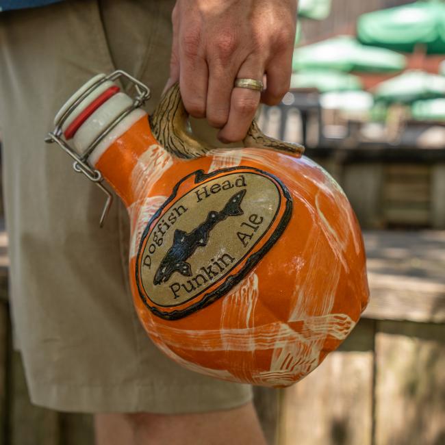 Person pictured carrying the orange growler with Dogfish head logo centered with writing 